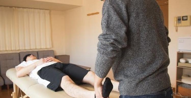 A man on a physio table, with a physio wearing a grey jumper holding his foot