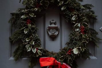 A grey door with a green and red Christmas wreath