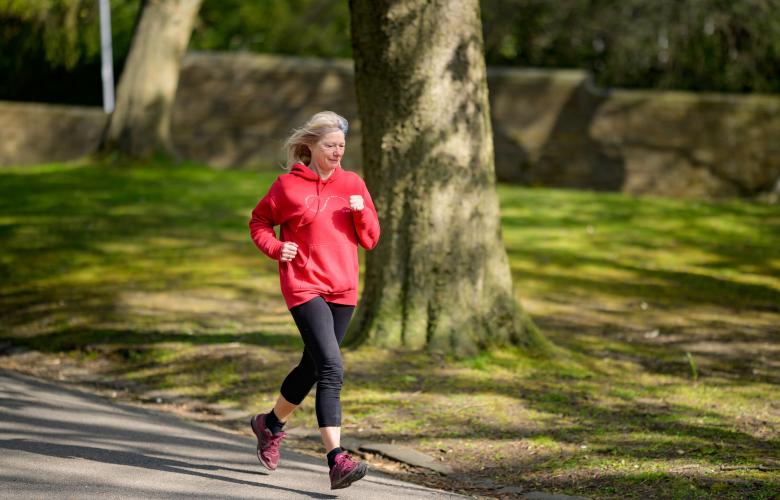 a woman with grey hair running through a park. she is wearing a red hoodie and black leggings. 