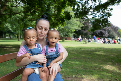 A mum is sitting in a park with two twin girls on her lap 