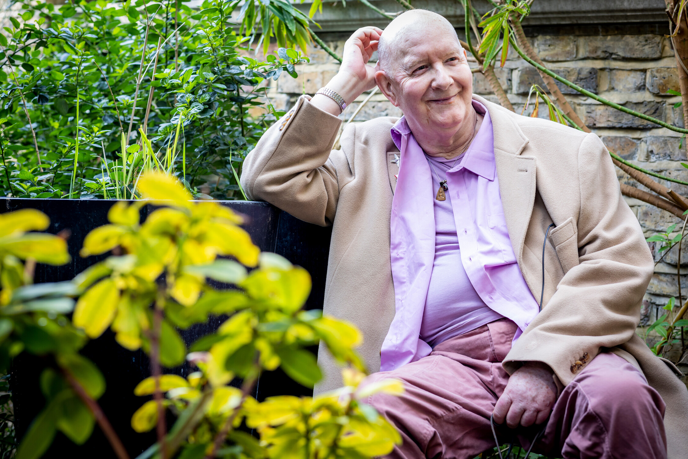 A man sits outside with green bushes and plants surrounding him