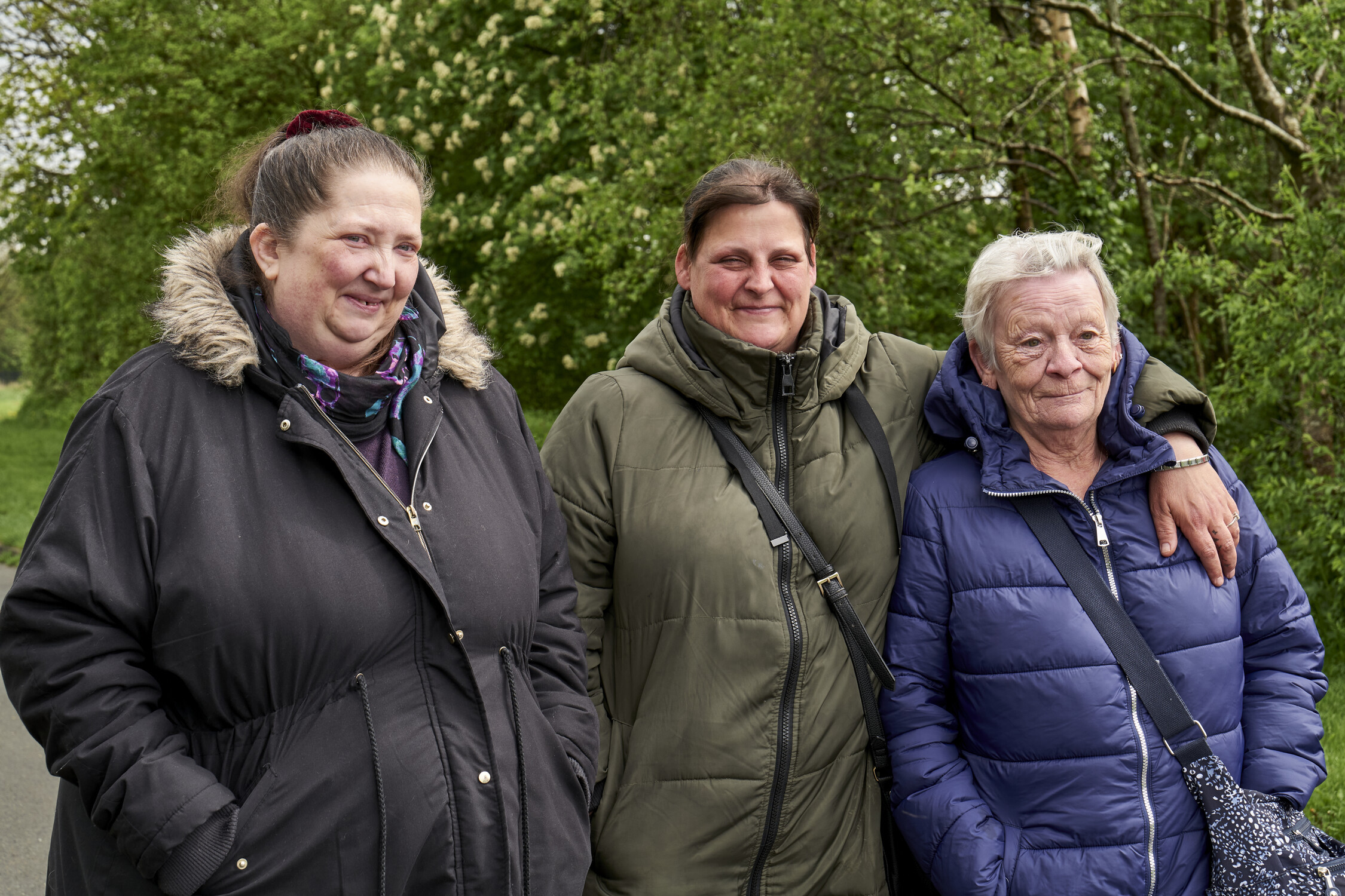 Three women are outside wearing winter coats, standing together and linking arms 