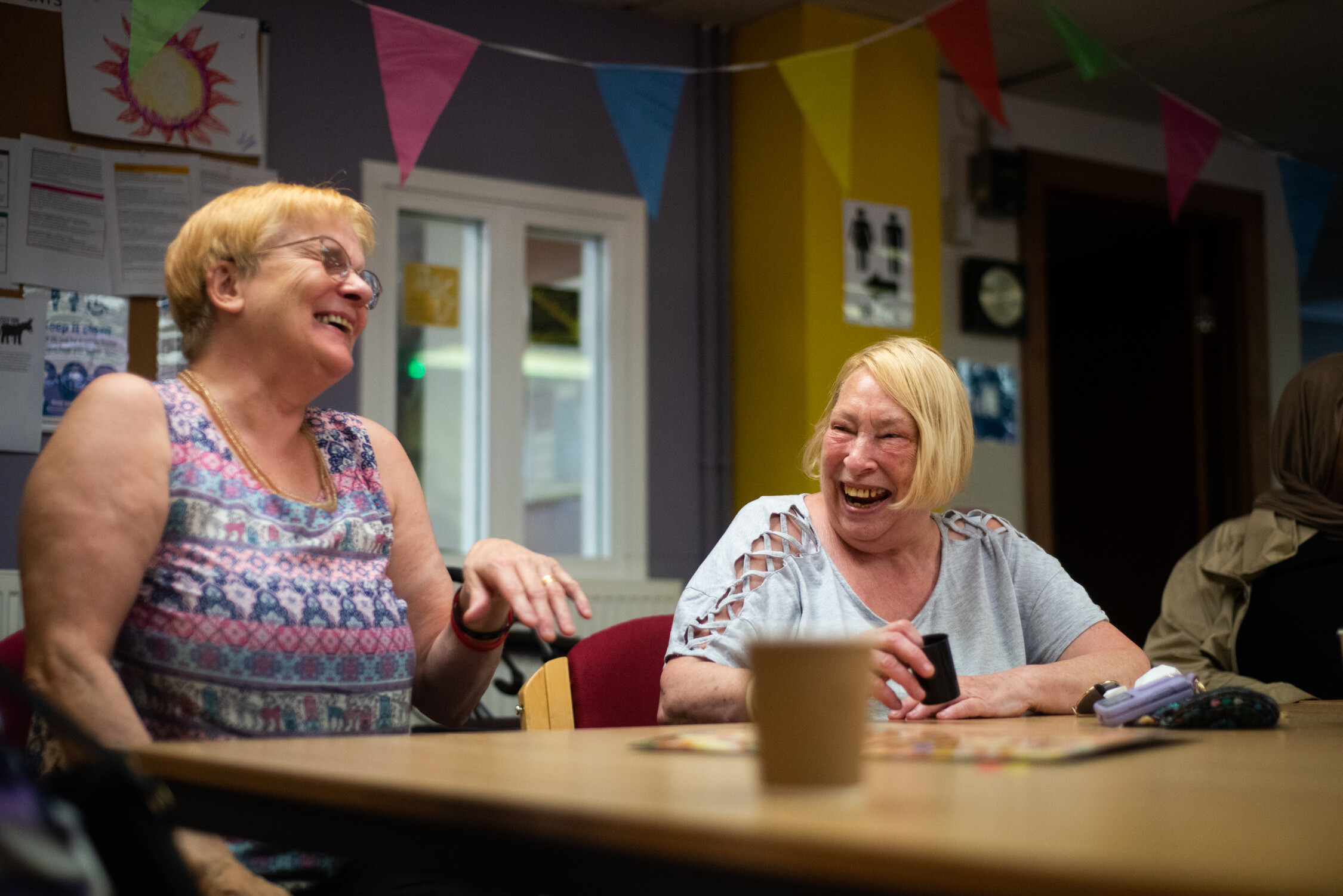 Two women sit together smiling in a brightly-decorated room with bunting