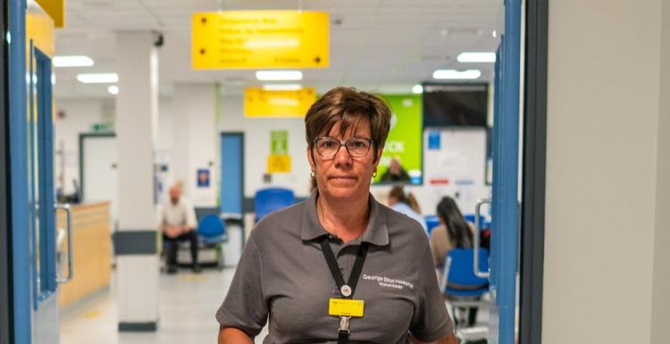 A woman wearing a grey t shirt walking through a hospital corridor