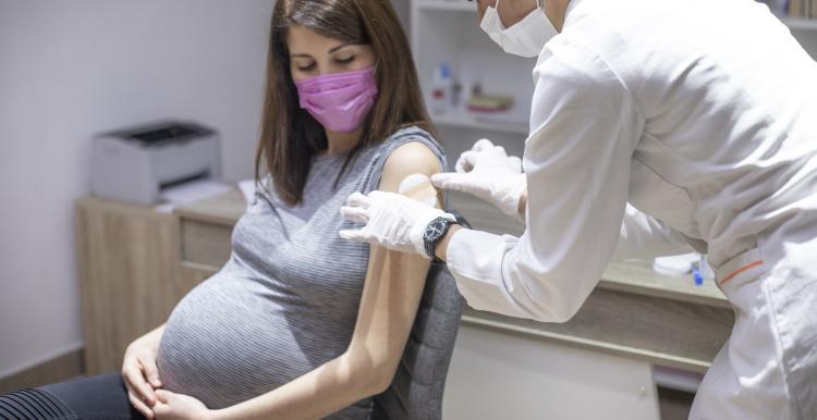 A pregnant woman sits on a chair with a nurse by her side