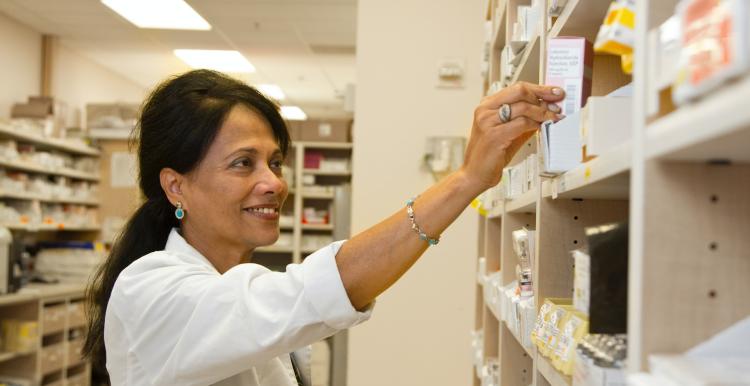 A female pharmacist in a white coat puts medicines on a shelf