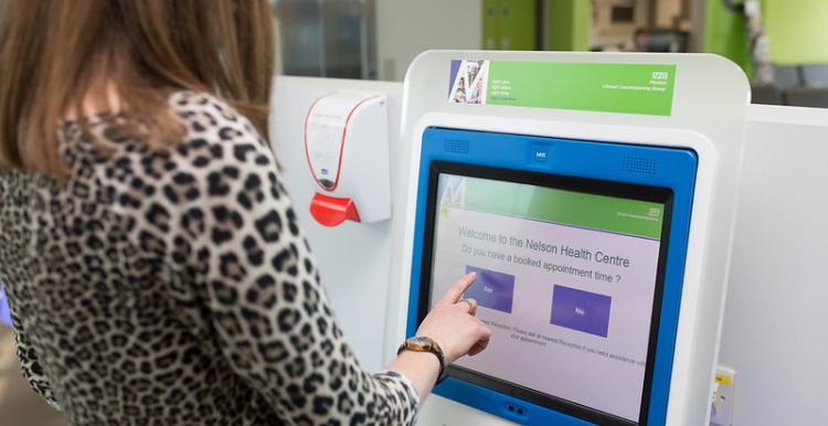 A woman wearing a leopard print top and long blonde hair standing at a doctor's reception check in screen