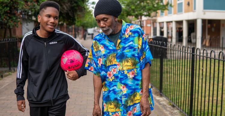 A young boy holding a pink football talking to an older man with a grey beard and a bright blue tropical print shirt