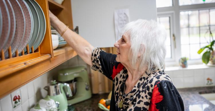A woman with white hair stacking plates in a kitchen