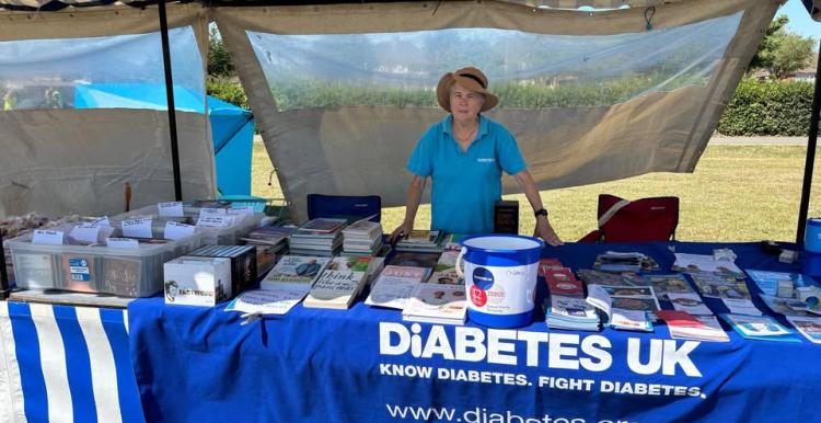 A woman wearing a blue t shirt standing outside in front of a stall with leaflets and books. A Diabetes UK blue banner is in the foreground.