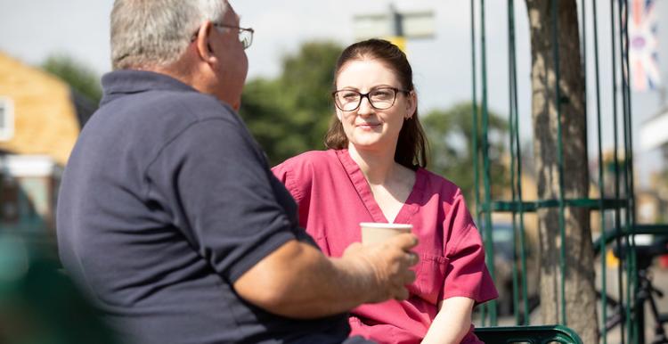 A man wearing a blue t shirt is sitting next to a doctor in red scrubs