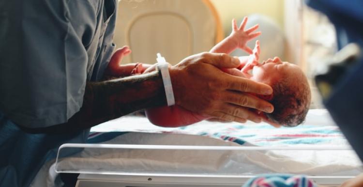 A doctor holds a newborn baby above some scales 