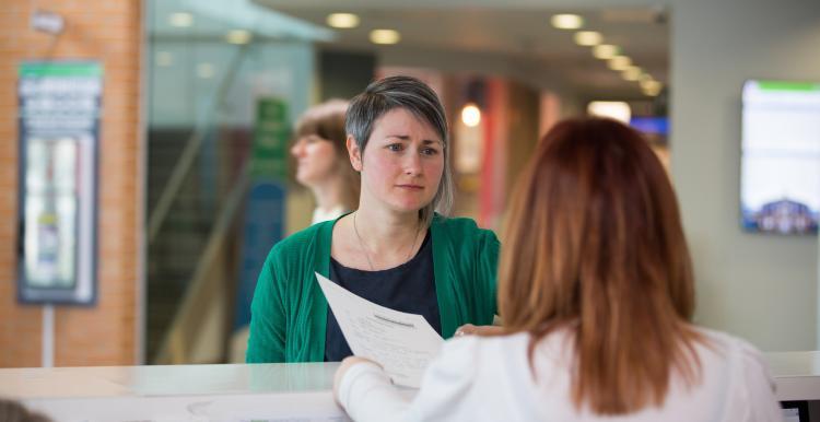 A woman stands at a hospital reception desk 