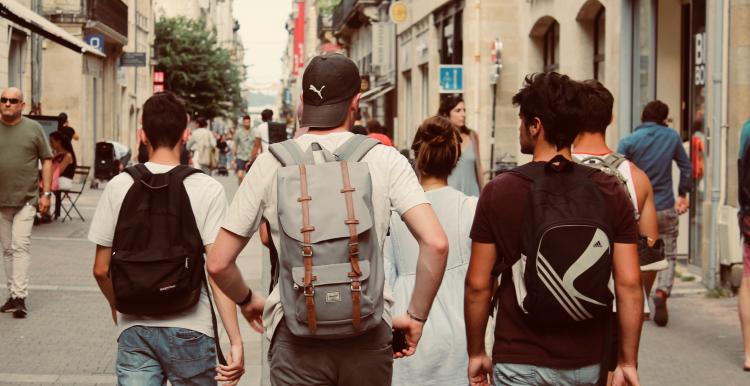 Five teenagers walk along a street wearing backpacks 