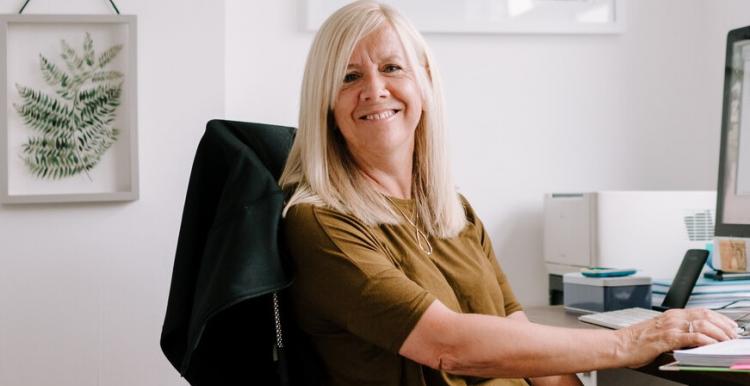 A woman sits at her desk and smiles at the camera A woman sits at her desk and smiles at the camera