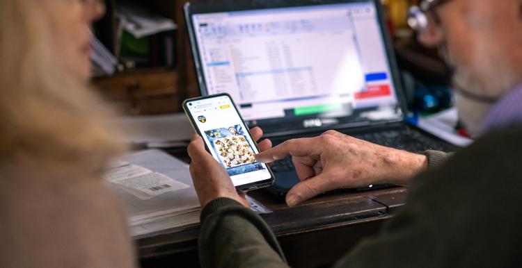 Close up of a man wearing glasses looking at a laptop and phone screen