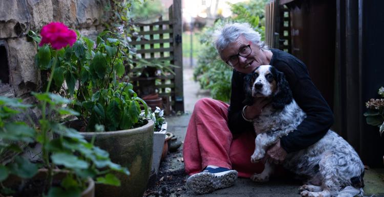 An elderly woman sits outside with her dog