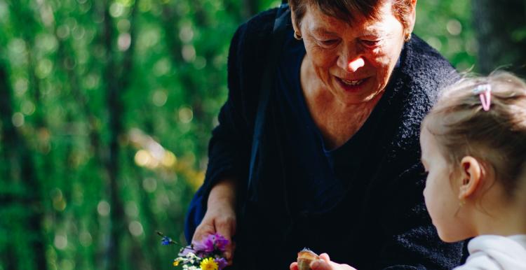 An older women shows a young girl a shell and a flower outdoors 