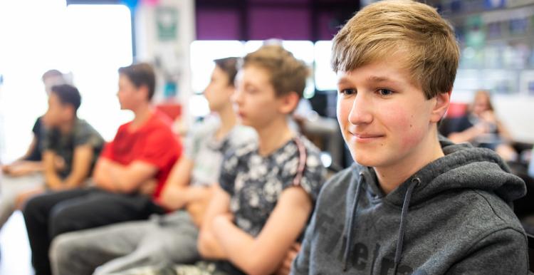 Teenage boy sitting with four other boys who are looking away from the camera