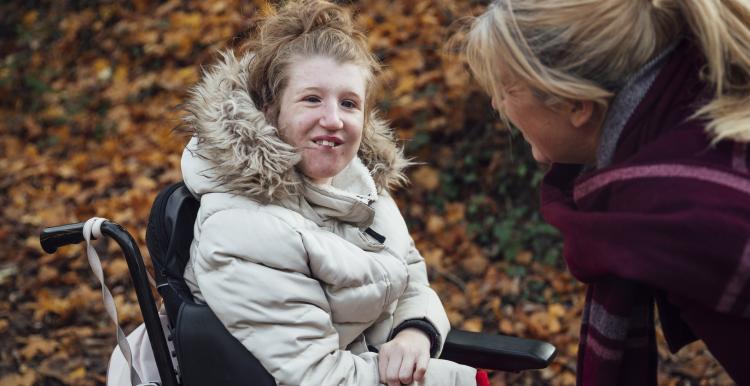 Young woman wearing a winter coat sitting in a wheelchair outside.