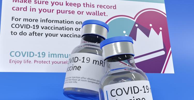 A COVID vaccine card and a vaccine bottle against a blue background