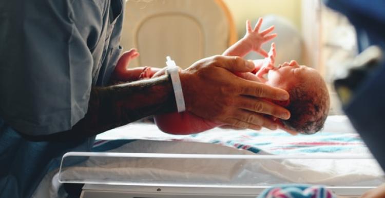 A close up of a nurse in scrubs holding a new born baby 