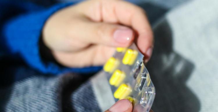 A close up of hands holding a blister pack of yellow pills