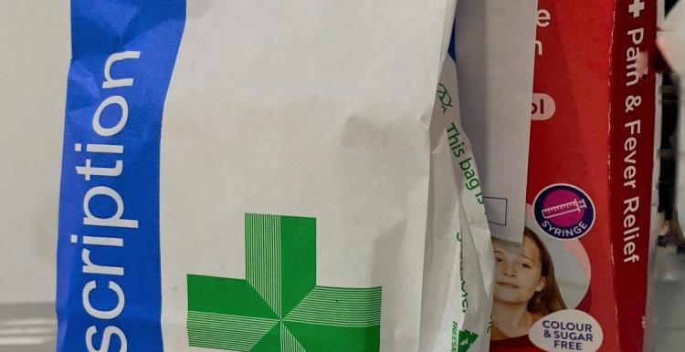 A white and blue paper bag with a green cross on it, and the word 'prescriptions' in white text.