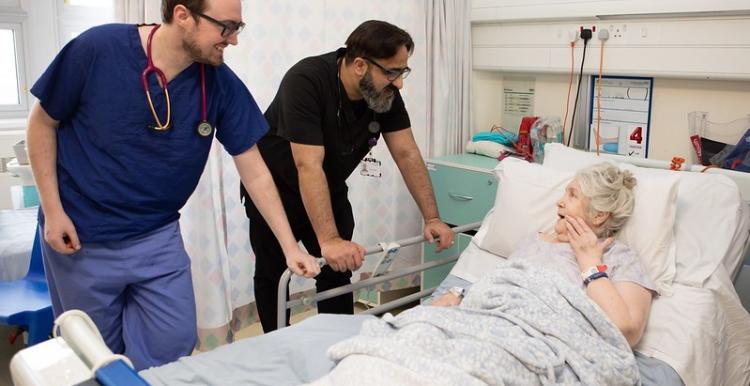 Two male doctors talking to a woman in a hospital bed