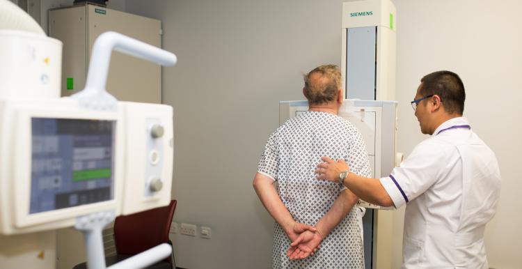 A man stands in front of a hospital screening machine next to a doctor