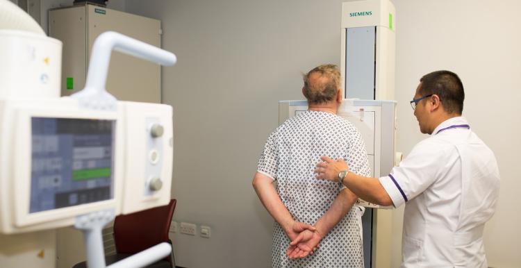 A man stands in front of a hospital screening machine next to a doctor 