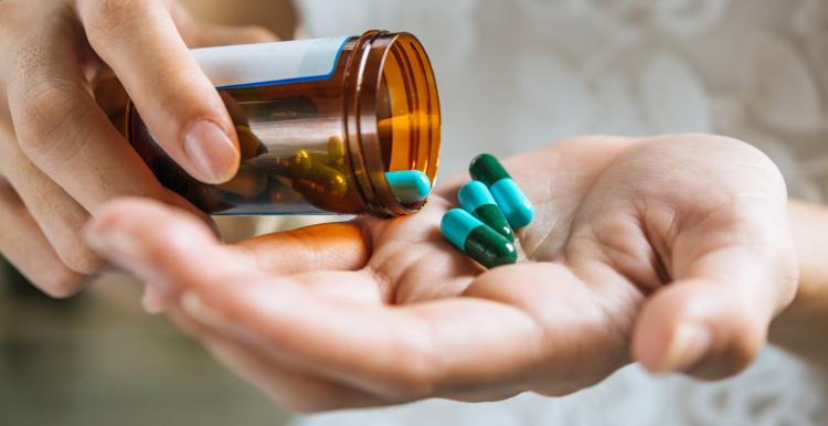 Hands holding a medicine bottle with green pills