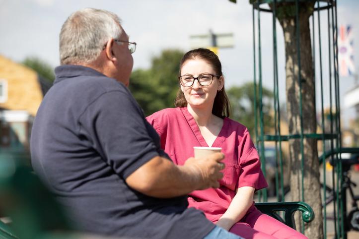 A man wearing a blue t shirt is sitting next to a doctor in red scrubs