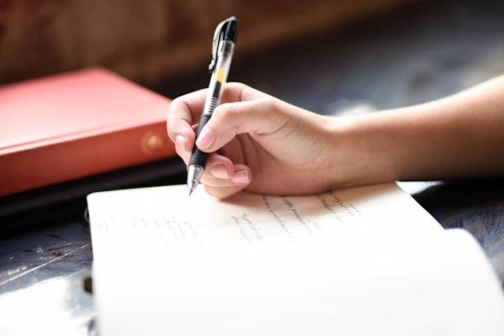 A close up of someone holding a pen and writing in a notebook