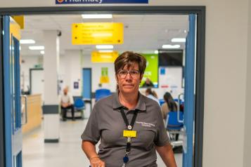A woman wearing a grey t shirt walking through a hospital corridor