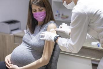 A pregnant woman sits on a chair with a nurse by her side