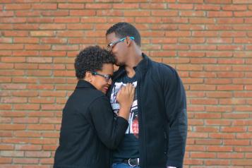 A man and woman standing in front of a brick wall hugging 