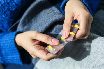 A close up of someone holding yellow pills in their hands, wearing a bright blue jumper 