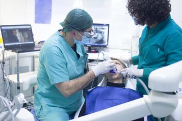 someone sitting in a dentist chair with a dentist next to them, surrounded by dental tools and equipment