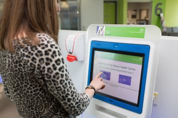 A woman wearing a leopard print top and long blonde hair standing at a doctor's reception check in screen