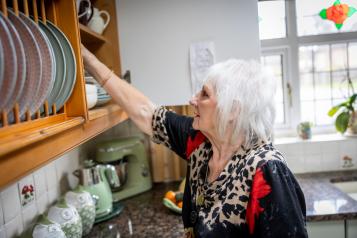 A woman with white hair stacking plates in a kitchen