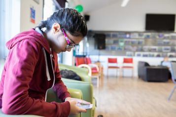 a teenage girl sits on a chair and looks down at her phone 