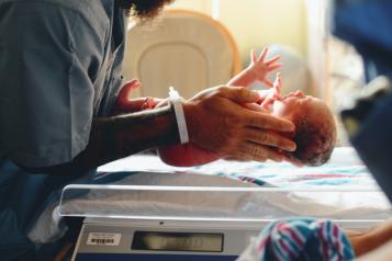 A doctor holds a newborn baby above some scales 