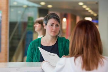 A woman stands at a hospital reception desk