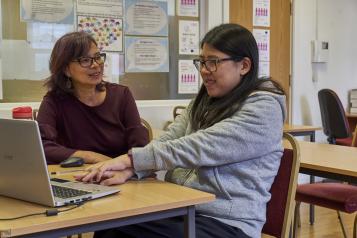 Two women are sitting in front of a laptop