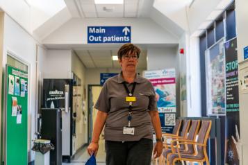 A woman with short brown hair walking along a hospital corridor. A blue sign above her head says 'Main Outpatients'  