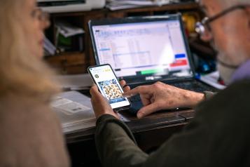 An elderly couple look at an iPad screen and a mobile phone