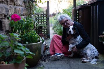 An elderly woman sits outside with her dog 