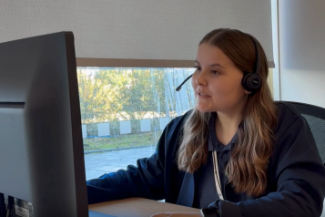 A woman sitting in front of a computer screen talking into a headset