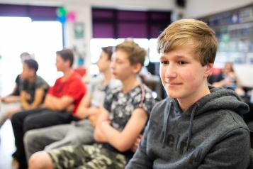 Teenage boy sitting with four other boys who are looking away from the camera